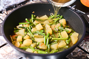 versare brodo su asparagi e patate in padella