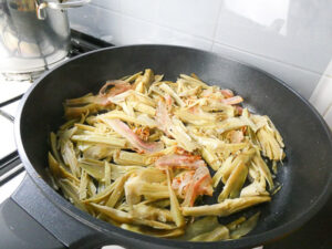aggiungere guanciale ai carciofi in padella